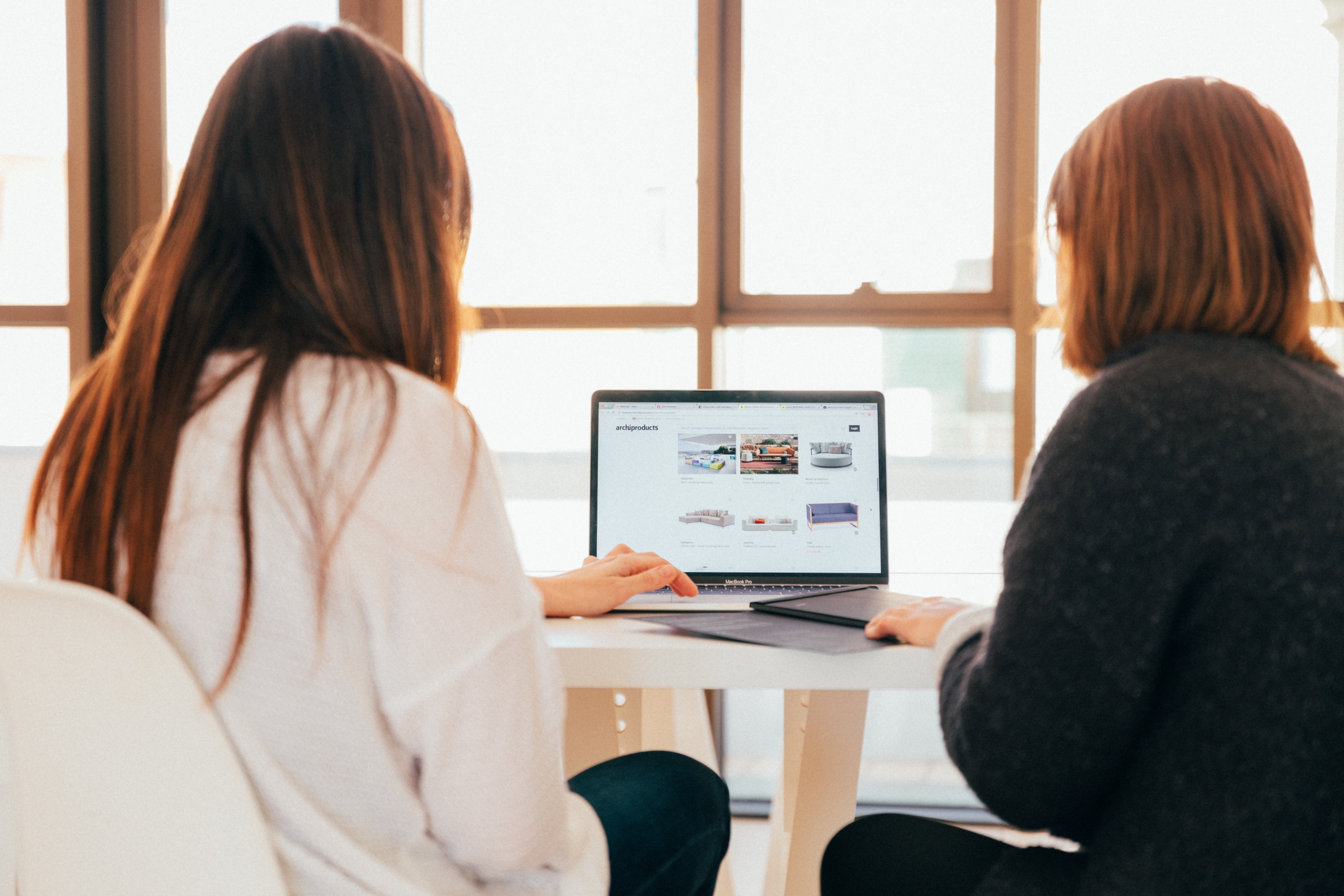 kobu-agency-7okkFhxrxNw-unsplash Two females looking at published catalogue pages on a laptop screen.